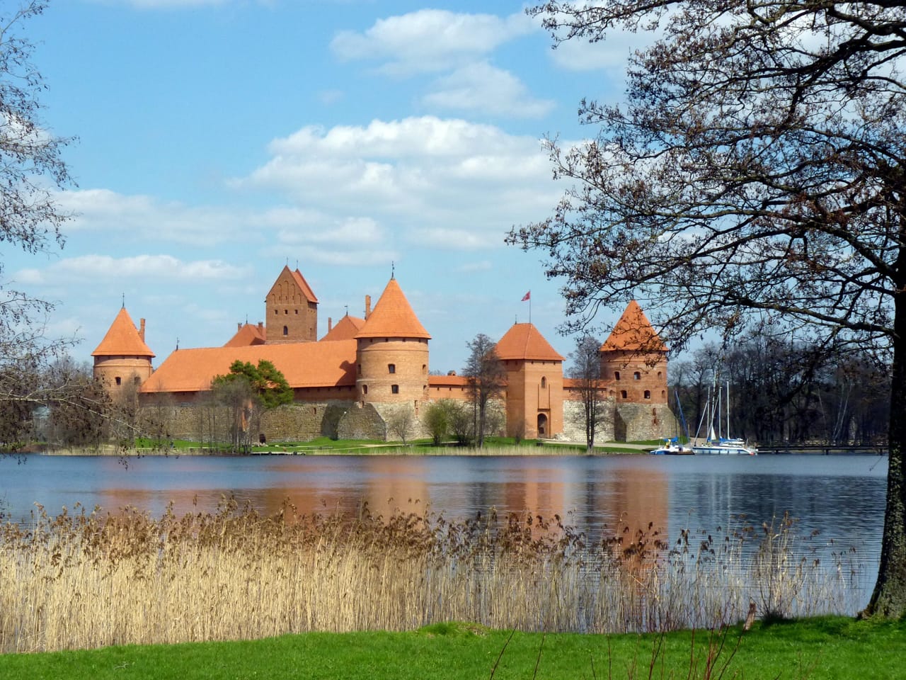 Het kasteel van Trakai en zijn spiegelbeeld in het Galvėmeer, onder blauwe lucht.