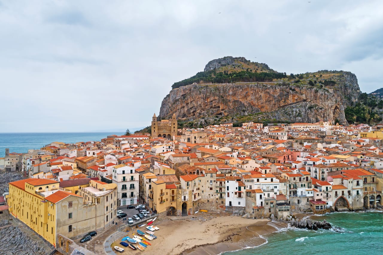 Cefalù au pied de la Rocca : les toits de la vieille ville, la cathédrale normande et la mer.