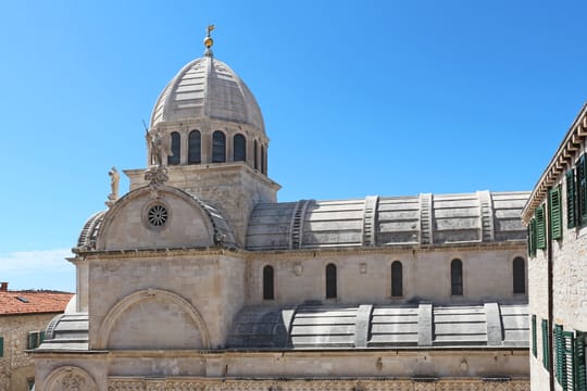 La cathédrale Saint-Jacques de Šibenik, sa coupole et sa nef de pierre, sous un ciel bleu.