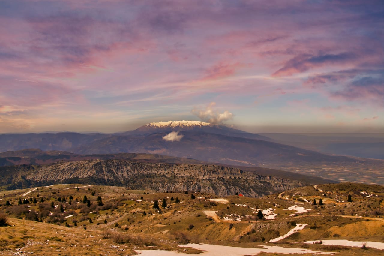 Le massif de l’Olympe et son sommet enneigé, sous un ciel rose au coucher du soleil.
