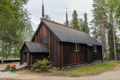 A velha igreja de madeira de Sodankylä, as suas telhas escuras e pináculos, sob os pinheiros.
