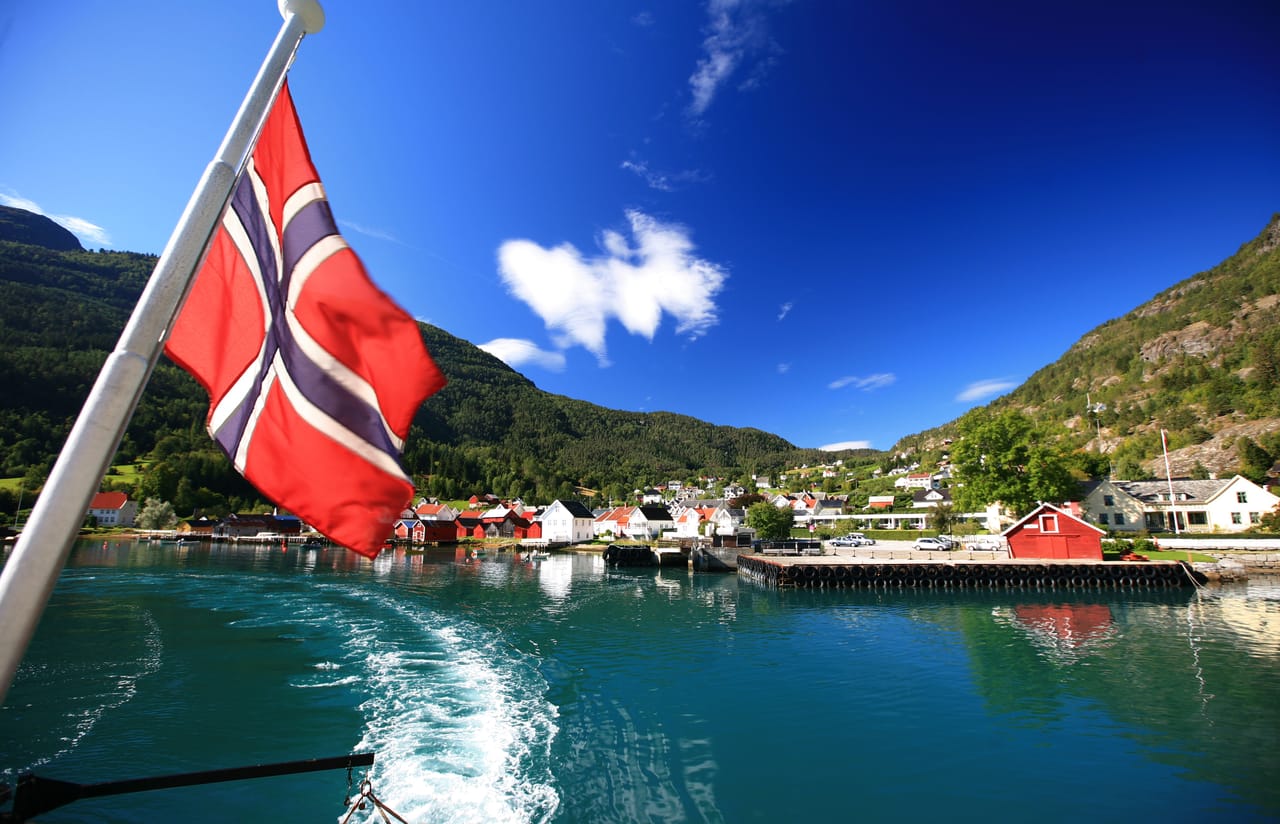Solvorn y sus casas de madera rojas y blancas a orillas del Lustrafjord, bajo un cielo azul.
