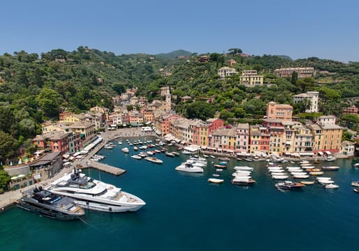 Portofino vu du ciel : le port en fer à cheval, les yachts et les façades peintes au pied de la colline boisée.