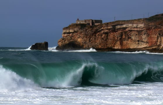 Une vague se creuse devant la falaise du Sítio et le fort de São Miguel Arcanjo, à Nazaré.