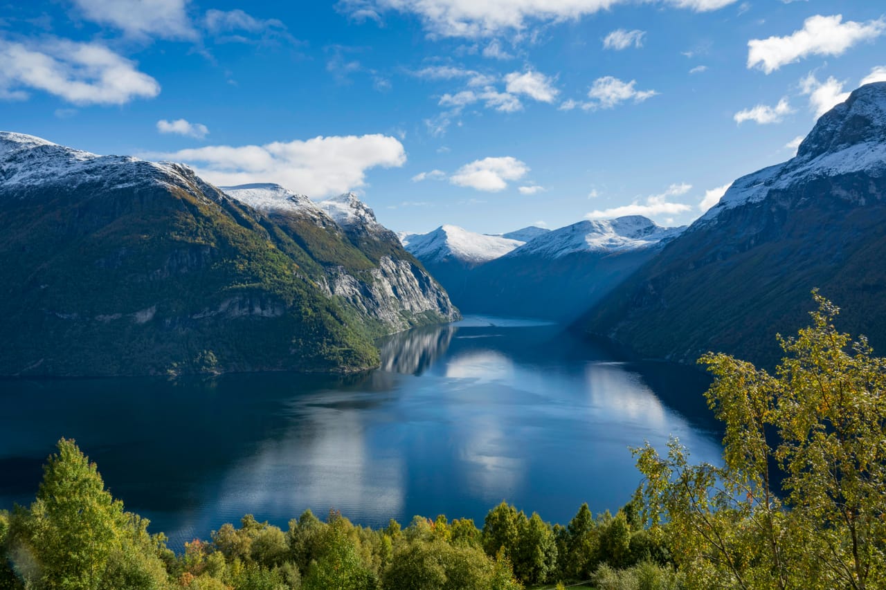 Le Geirangerfjord entre ses parois et ses sommets enneigés, sous un ciel bleu.