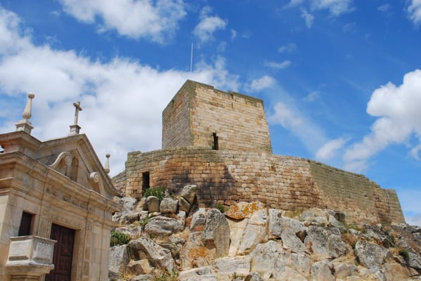 Le donjon de Marialva sur son chaos de granite, à côté du fronton d’une église.
