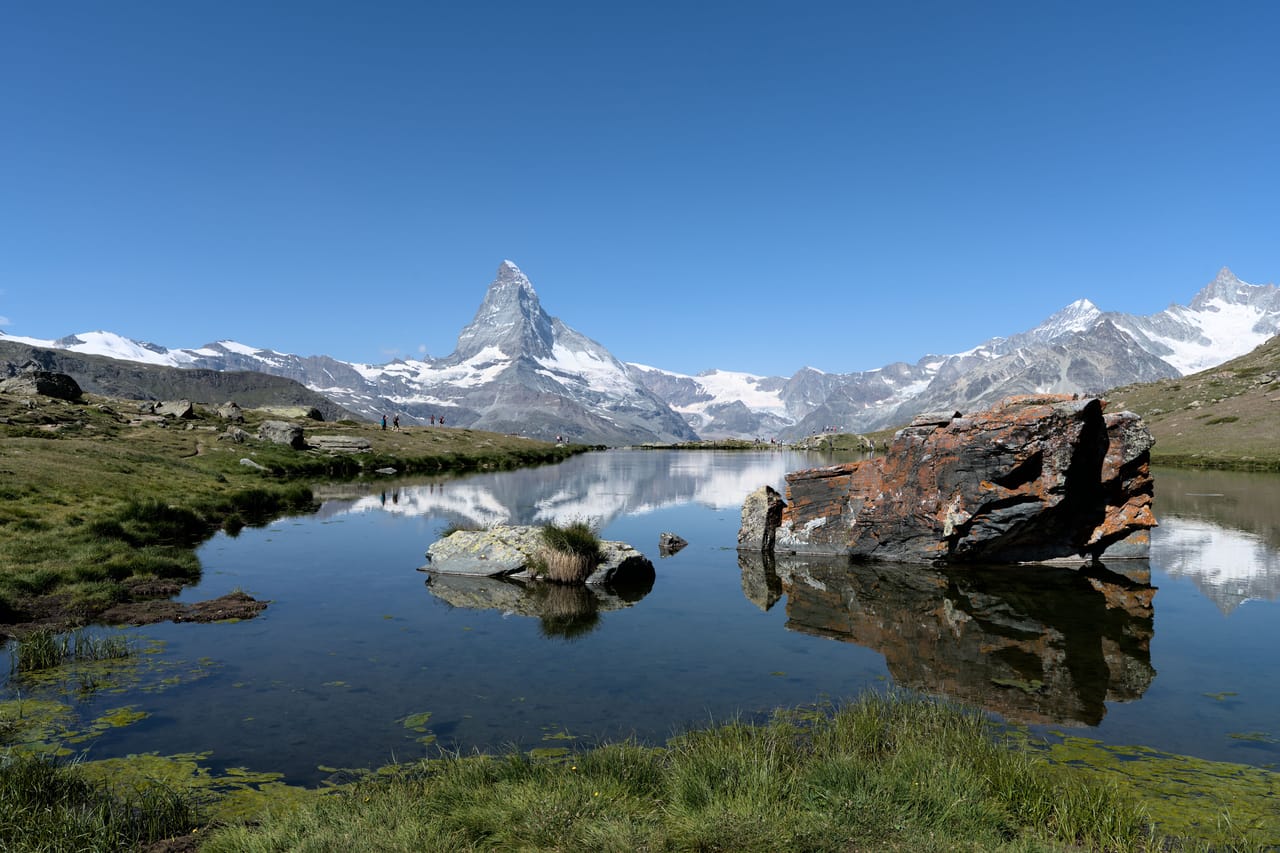 Le Cervin et les sommets de Zermatt qui se reflètent dans le Riffelsee, sous un ciel bleu.