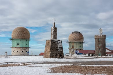 Le sommet de la Torre sous la neige : la tour de pierre surmontée d’une croix et les deux dômes d’une ancienne station radar.