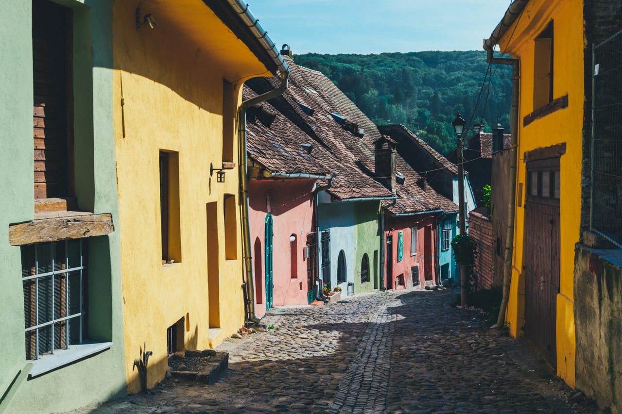 Une ruelle pavée de la ville haute de Sighișoara, entre maisons jaunes, roses et vertes.