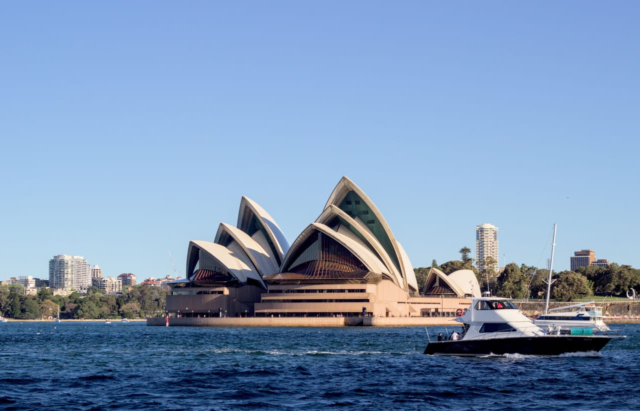 L’Opéra de Sydney au bord de la baie sous un ciel bleu, avec les bateaux au premier plan.