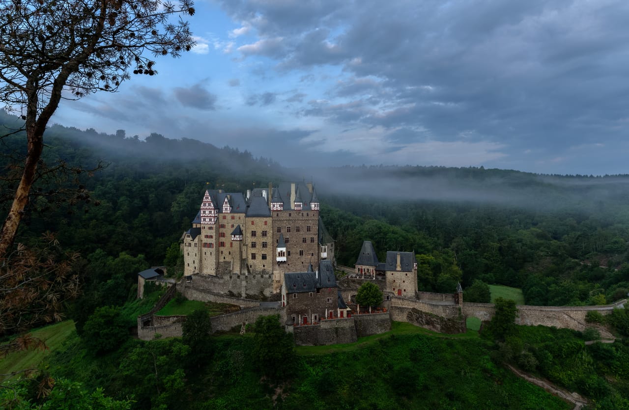 Burg Eltz no seu esporão rochoso, no meio da floresta, na neblina da manhã.