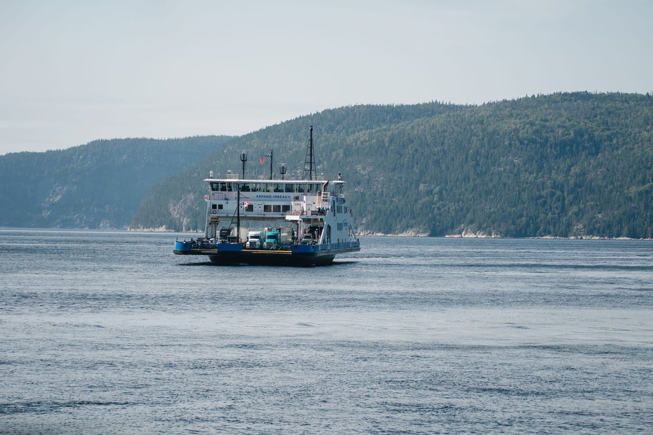Le traversier qui franchit l’embouchure du Saguenay à Tadoussac, entre les collines boisées.