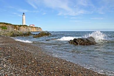 Le phare de Cap-des-Rosiers au bout d’une plage de galets.
