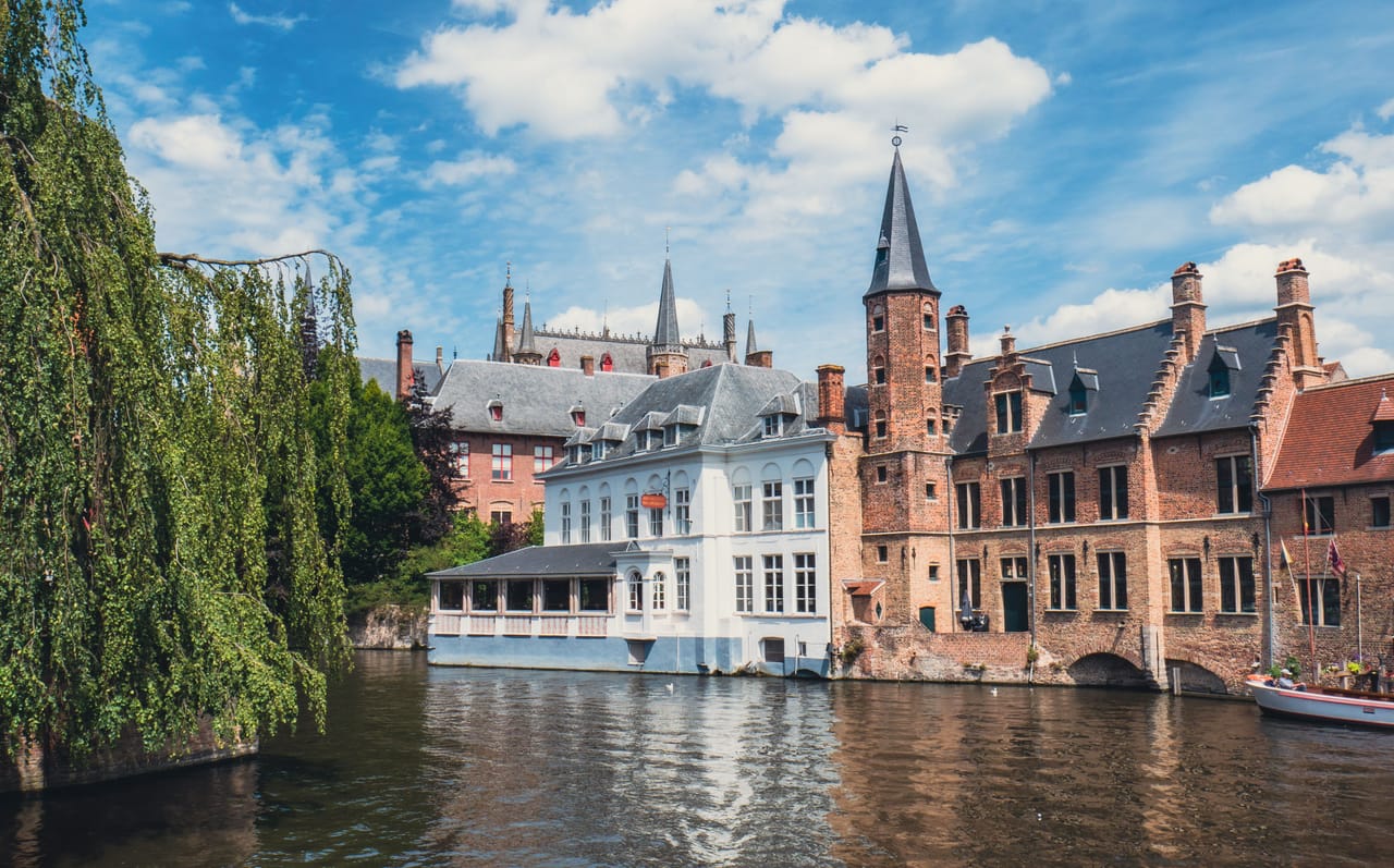 Un canal de Bruges, ses façades de brique et ses pignons à redents, sous le ciel bleu.